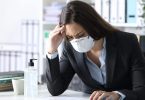 Worried bookkeeper with protective mask looking at calculator on a desk at the office