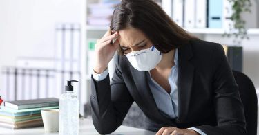 Worried bookkeeper with protective mask looking at calculator on a desk at the office