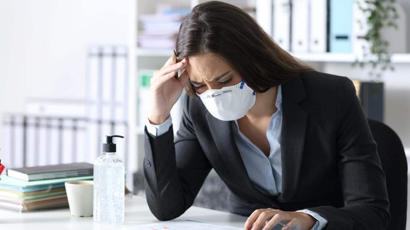 Worried bookkeeper with protective mask looking at calculator on a desk at the office
