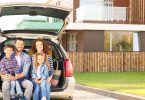 Young family with children sitting in car trunk near house