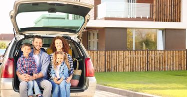 Young family with children sitting in car trunk near house