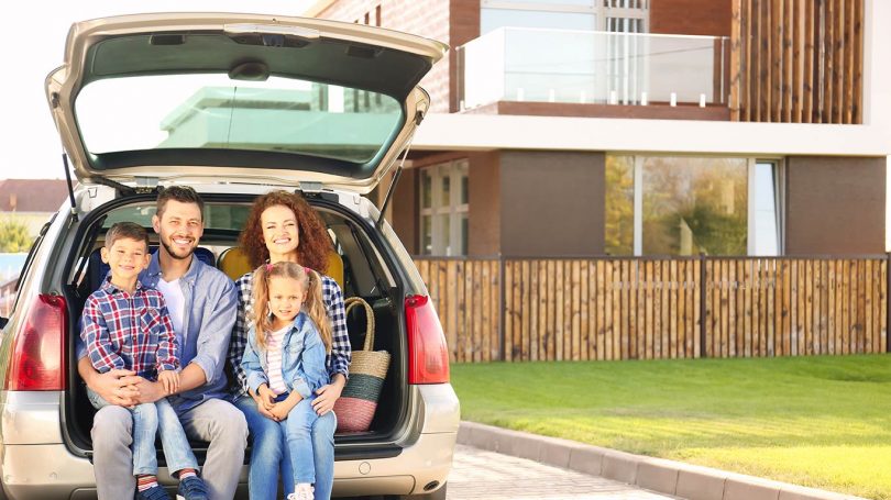 Young family with children sitting in car trunk near house