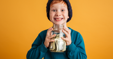 Photo of funny little redhead boy with freckles standing isolated over yellow background wearing warm hat.