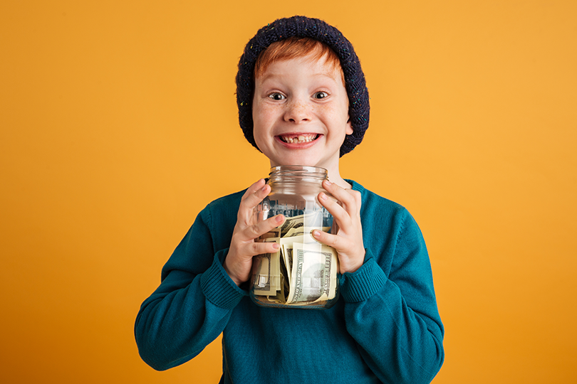 Photo of funny little redhead boy with freckles standing isolated over yellow background wearing warm hat.
