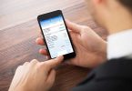 Close-up Of Businessman Doing Online Banking On Mobilephone At Office Desk
