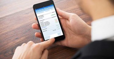 Close-up Of Businessman Doing Online Banking On Mobilephone At Office Desk