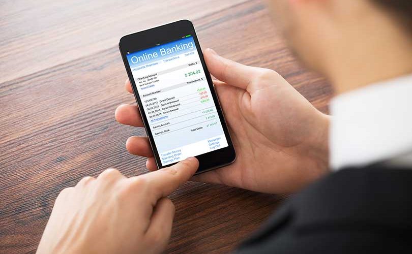 Close-up Of Businessman Doing Online Banking On Mobilephone At Office Desk