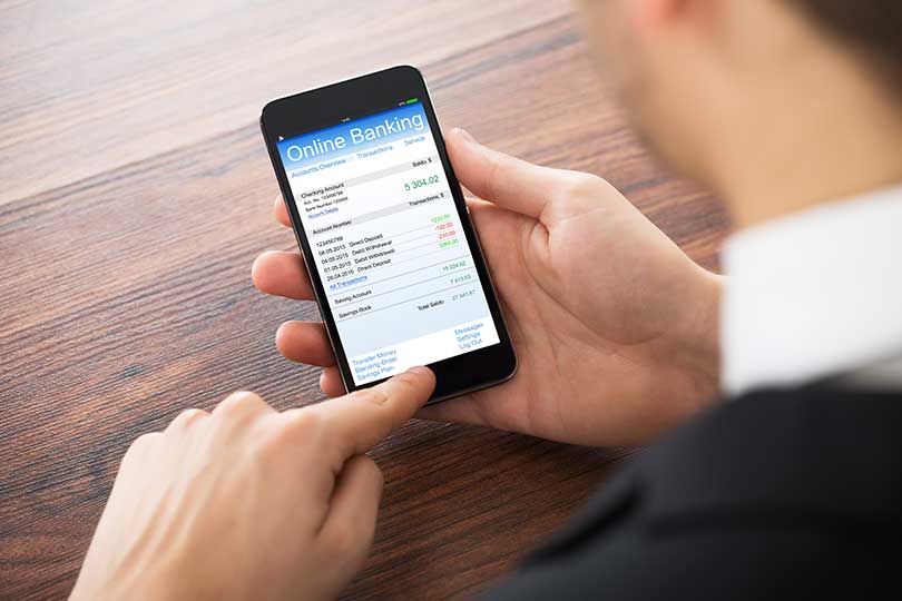 Close-up Of Businessman Doing Online Banking On Mobilephone At Office Desk